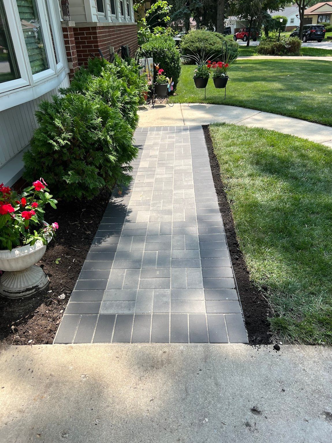 A brick walkway leading to a house with flowers on the side of it.