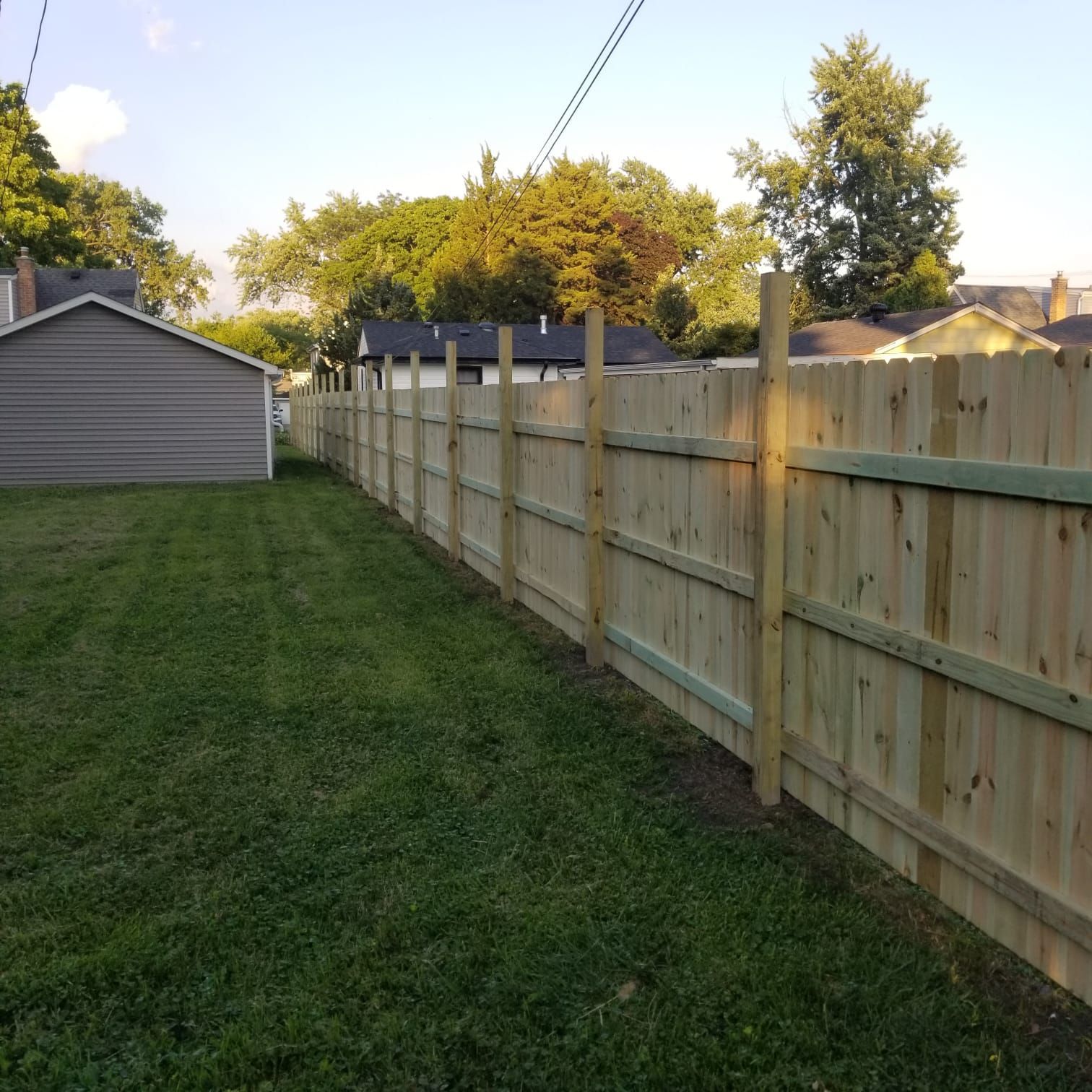 A wooden fence in a backyard with a shed in the background