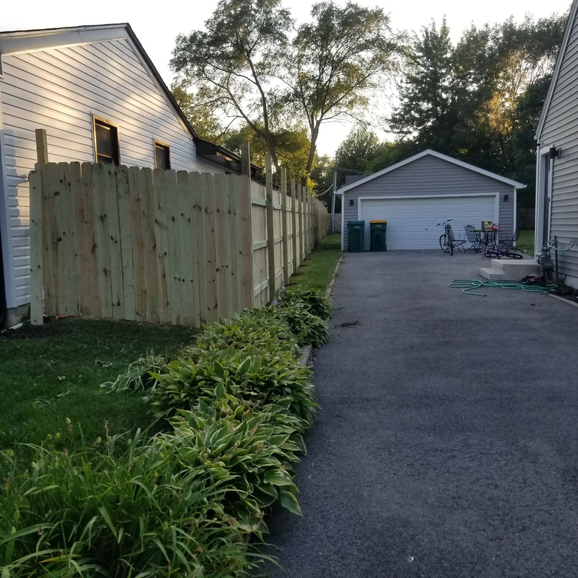 A wooden fence surrounds a driveway leading to a garage