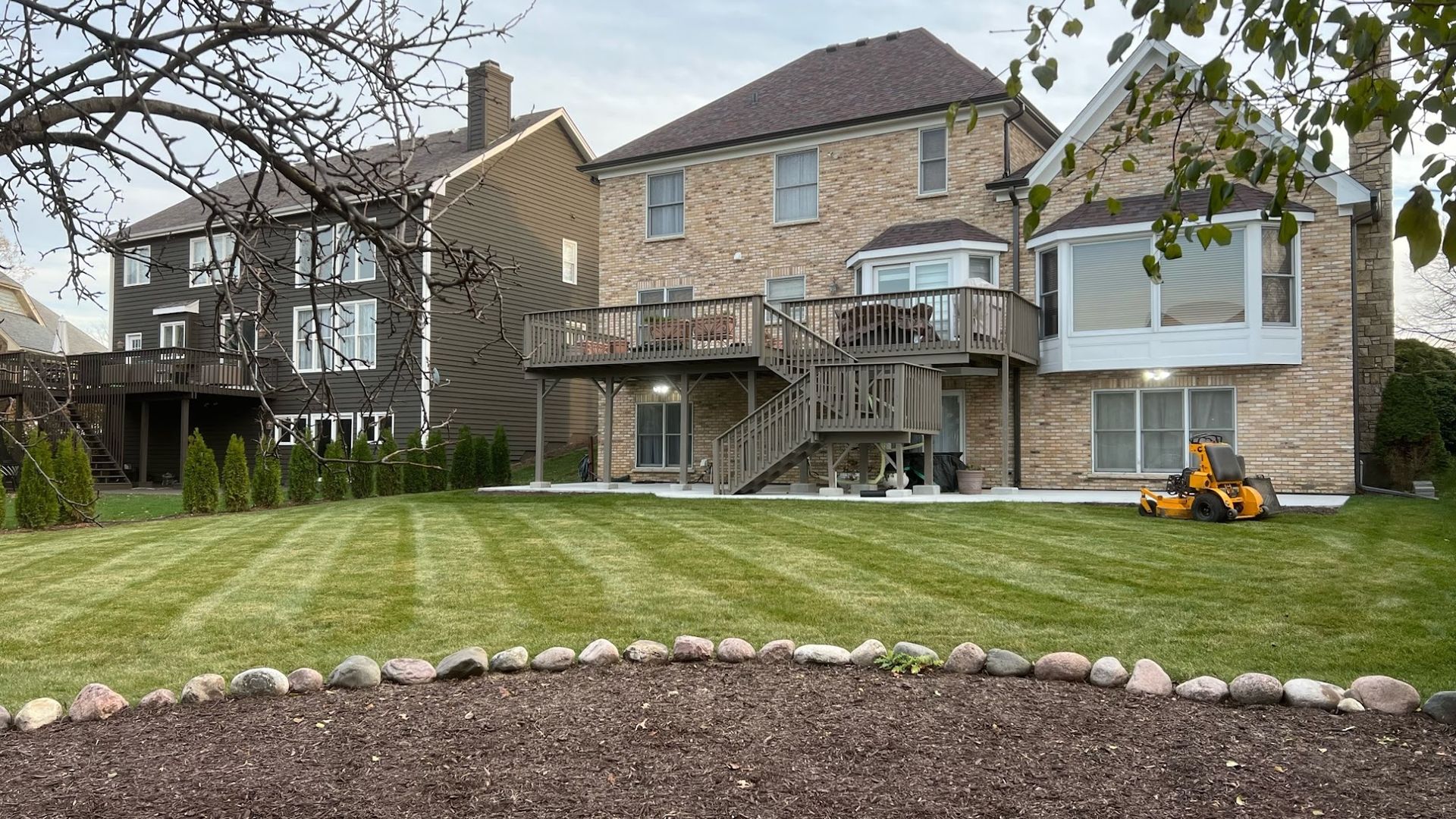 A lawn mower is cutting the grass in front of a large house.