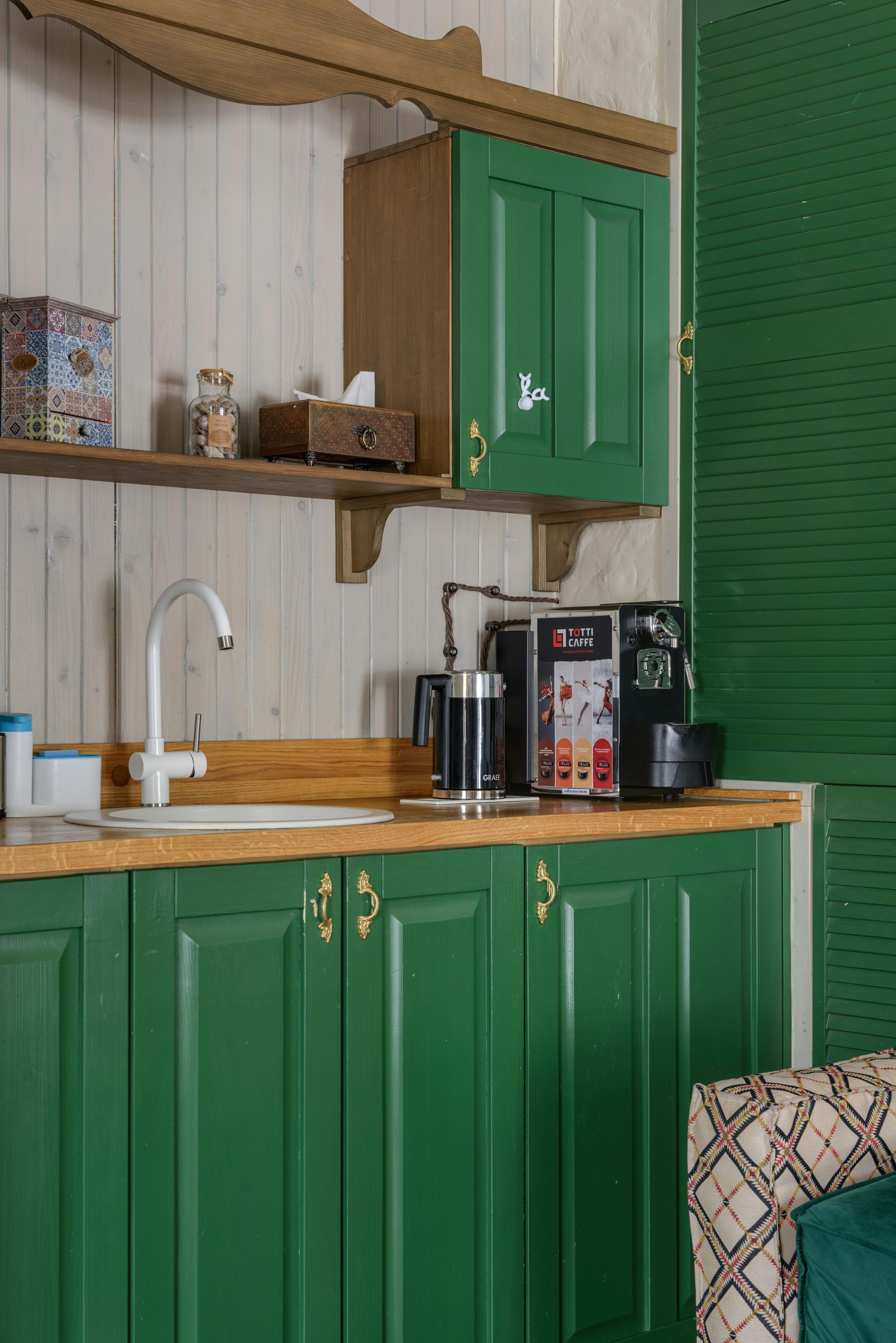 A kitchen with green cabinets , a sink , and a coffee maker.
