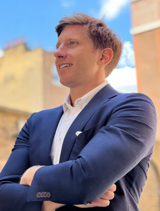 A man in a suit is smiling with his arms crossed