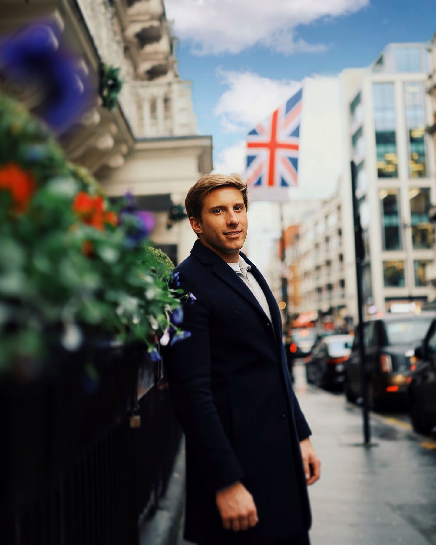 A man in a black coat is standing on a sidewalk in front of a british flag.