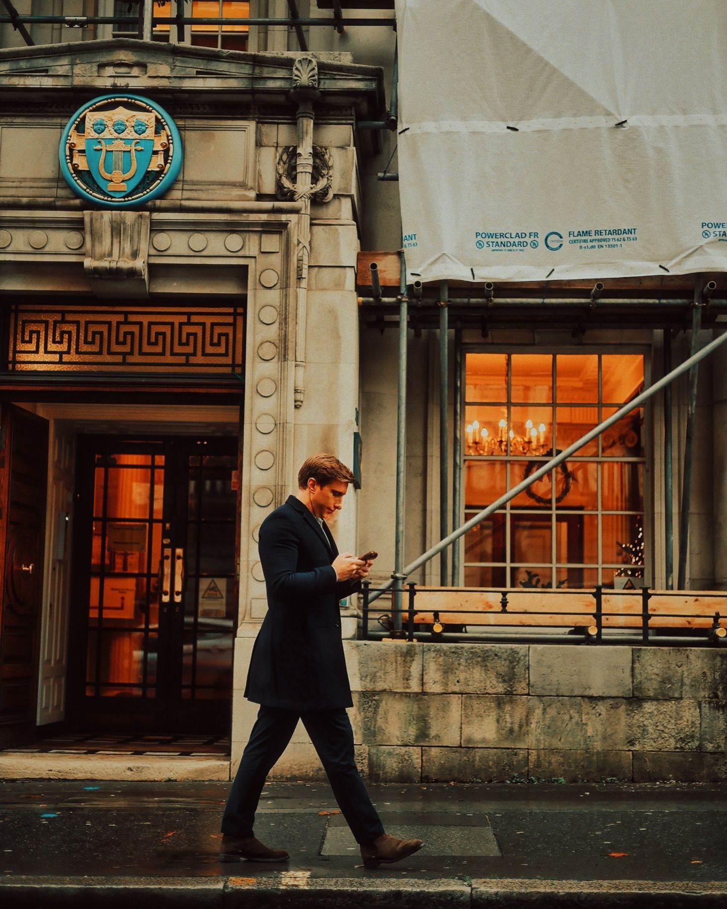A man walking down a sidewalk in front of a building that has the letter c on it