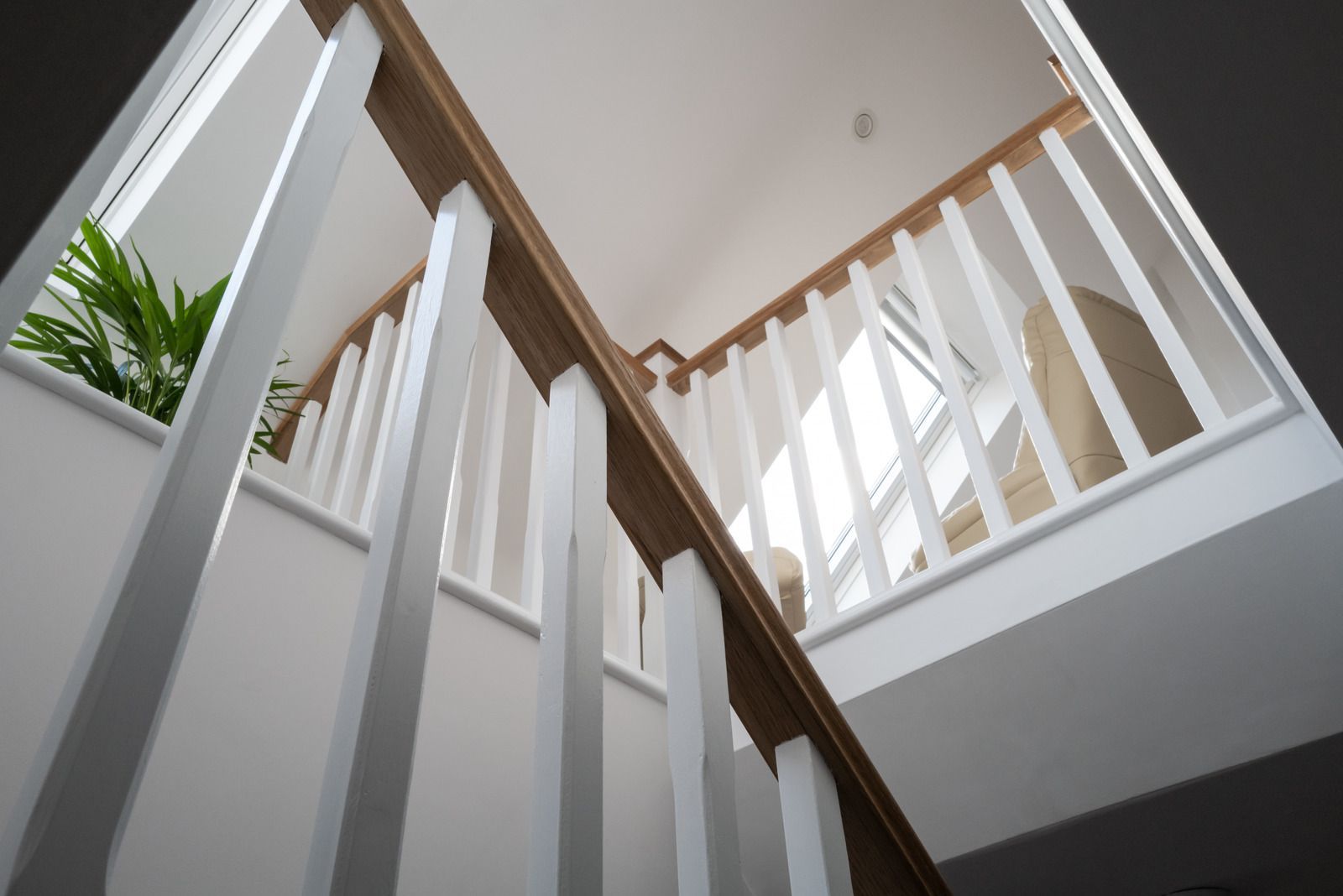 Looking up at a staircase with white railings and wooden handrails