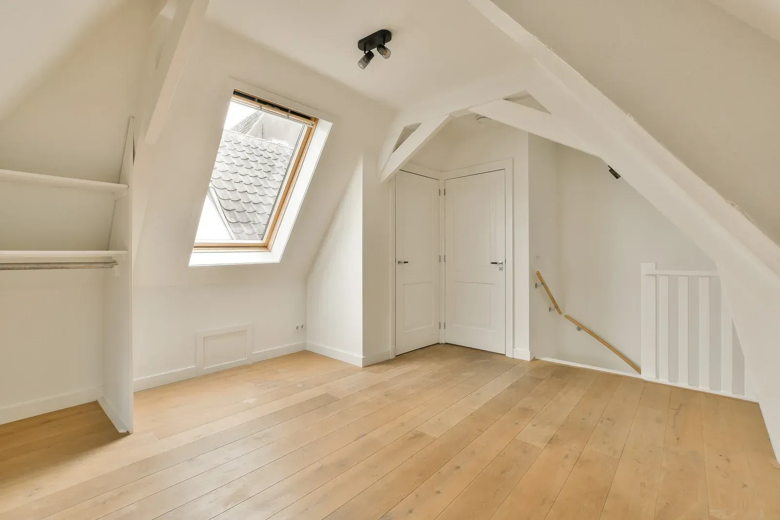 An empty attic with hardwood floors and a skylight.