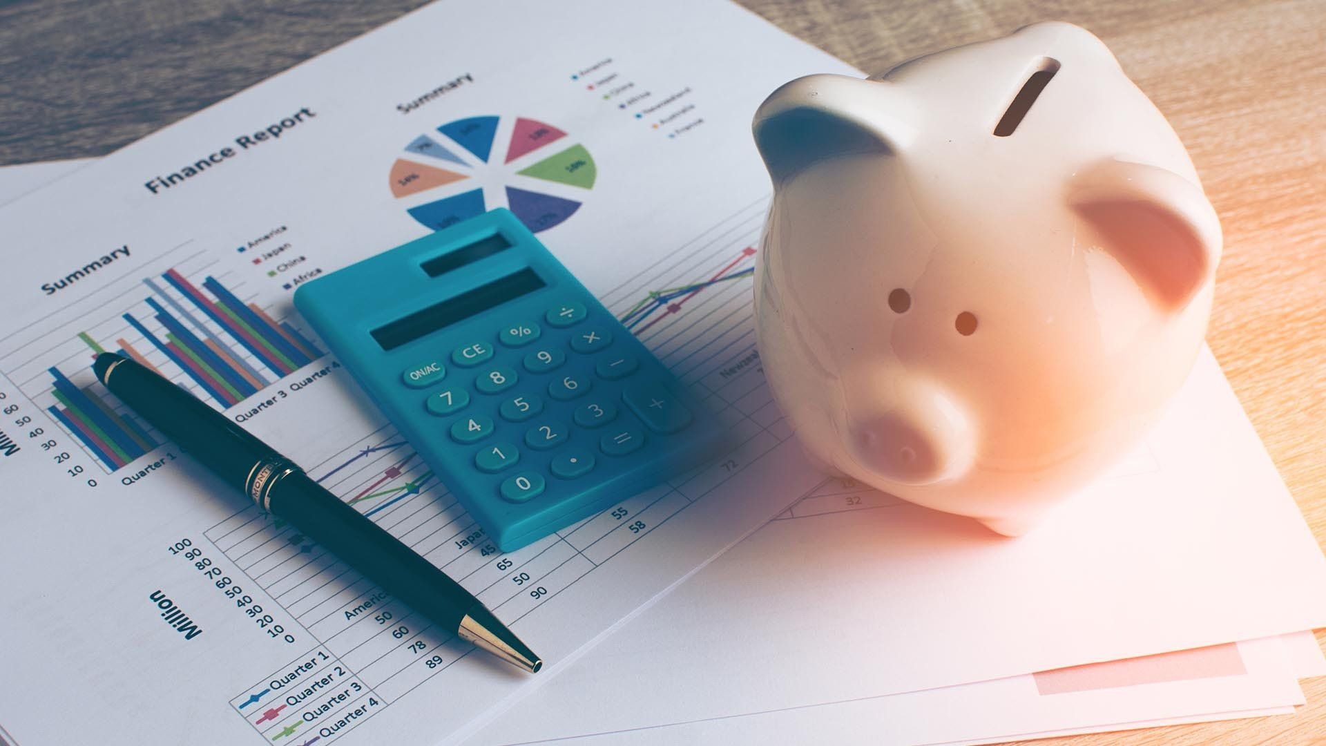 calculator, pen, and piggy bank on a paper that has financial information