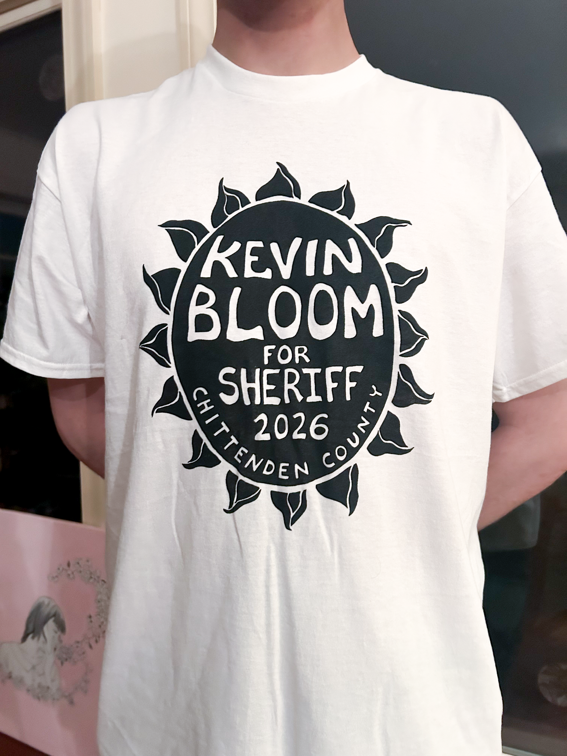 A person wears a white t-shirt featuring a black sunflower graphic with the text 