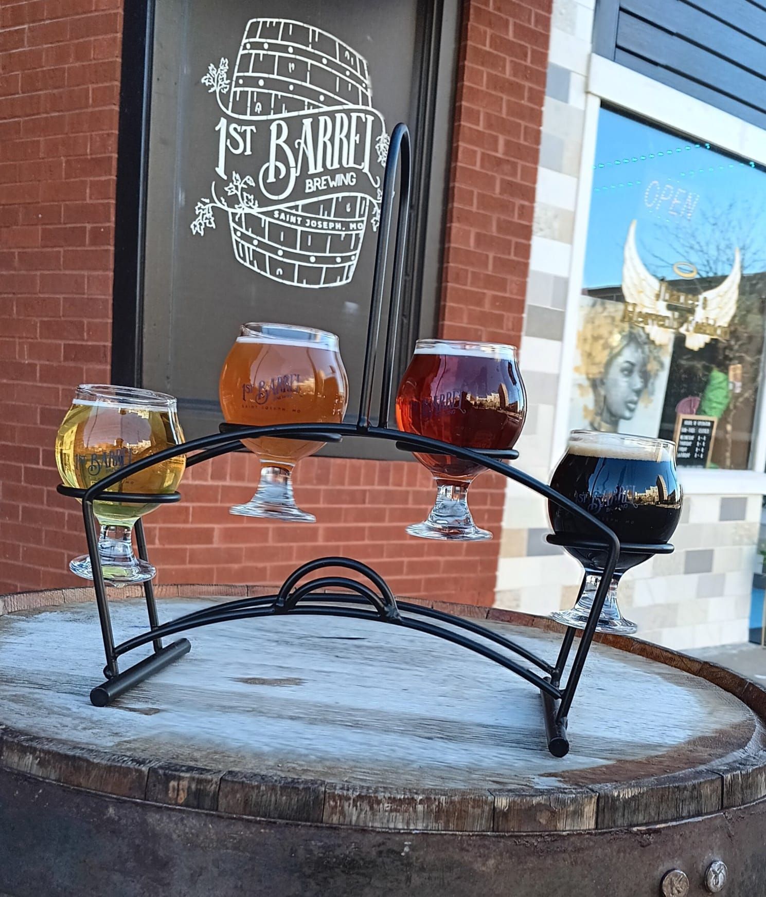 Four glasses of beer are sitting on top of a wooden barrel.