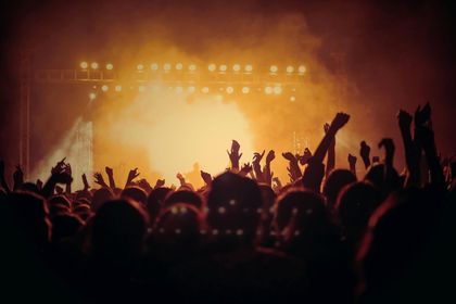 Crowd at a concert with hands raised toward a brightly lit stage.