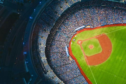 Aerial view of a baseball stadium packed with fans, focusing on the green field and red dirt infield.
