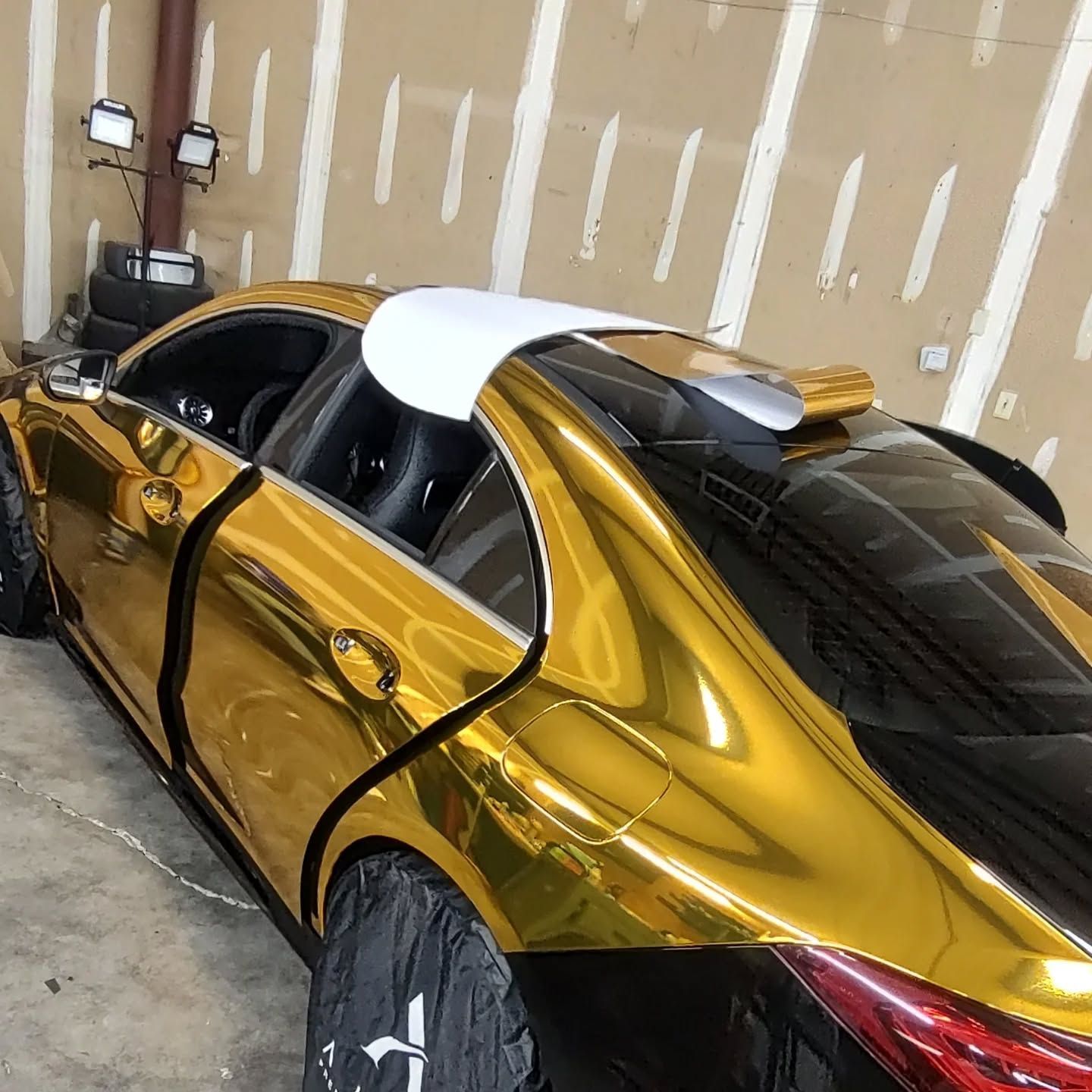 Gold-wrapped car with black accents in a garage, doors open, partially covered tires.