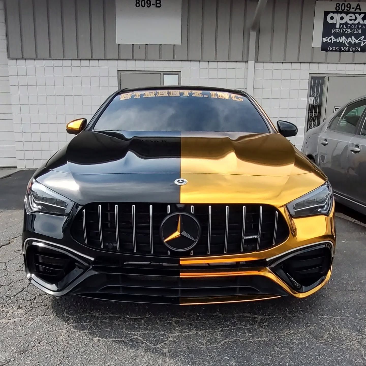 Black and gold split color Mercedes-Benz CLA parked in front of a building.