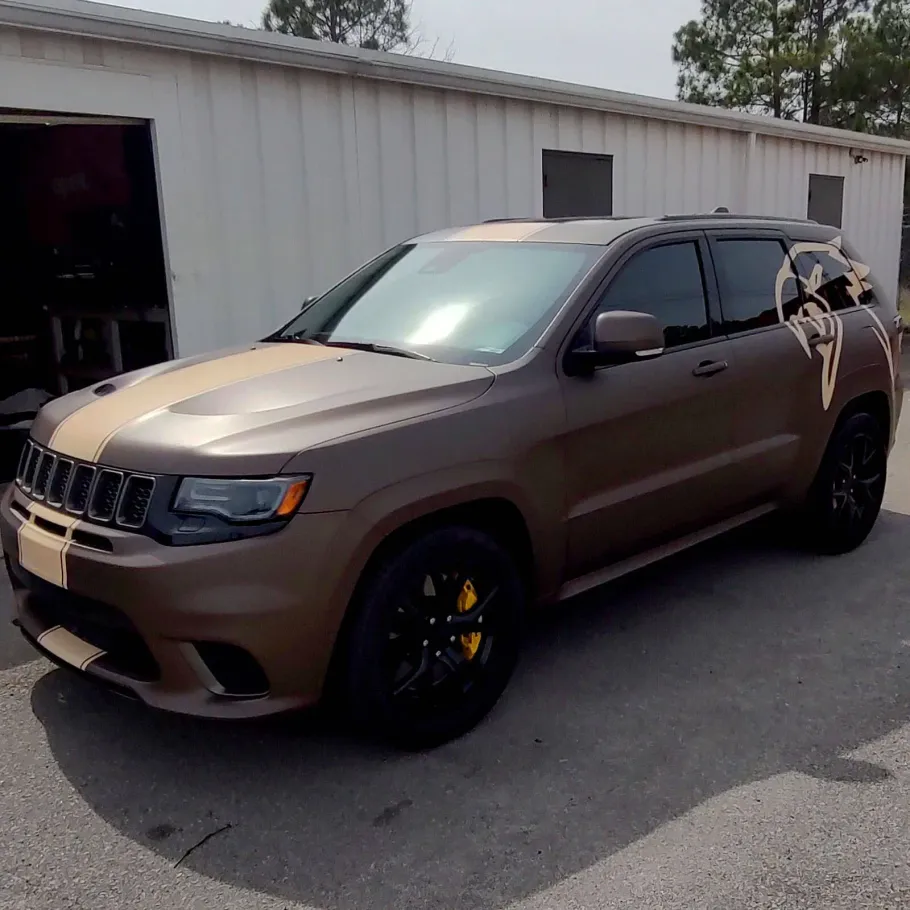 Brown Jeep Grand Cherokee with racing stripes, parked outside a garage.