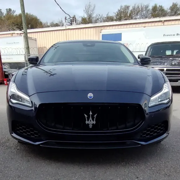 Dark blue Maserati sedan parked outdoors with the Maserati trident logo on the front grill.