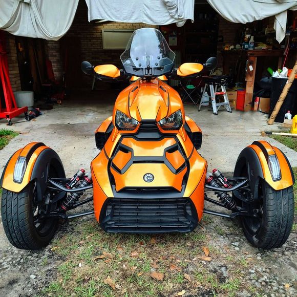 Orange Can-Am Ryker three-wheel motorcycle, parked on a driveway in front of a garage.