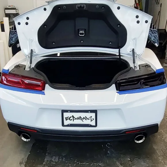 White car trunk open, revealing the interior. Black accents, blue tape, and license plate visible.