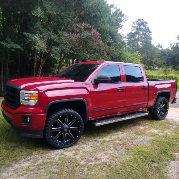 Red GMC pickup truck parked on grass with black rims and tinted windows.