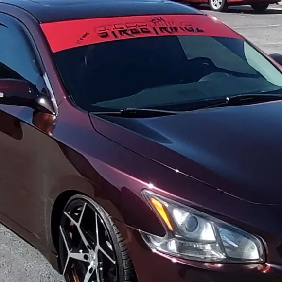 Dark red car with black rims and a red windshield banner that says 