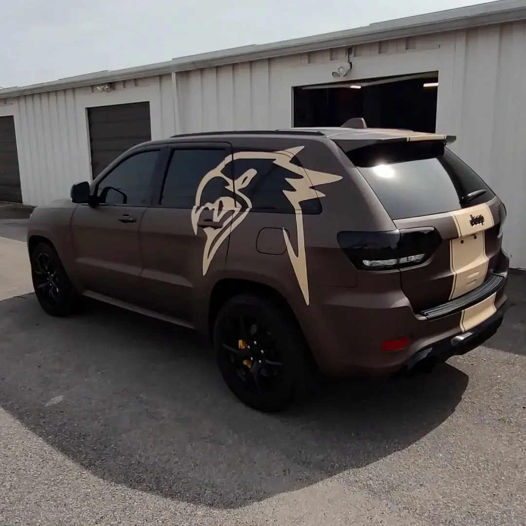 Brown Jeep SUV with tan stripes and a large logo, parked outside a building.