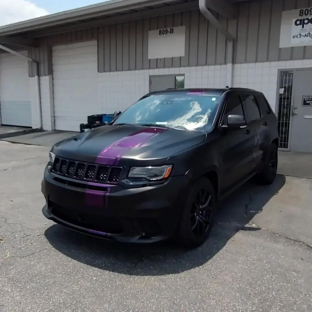 Black Jeep SUV with purple racing stripe, parked in front of a building with garage doors.