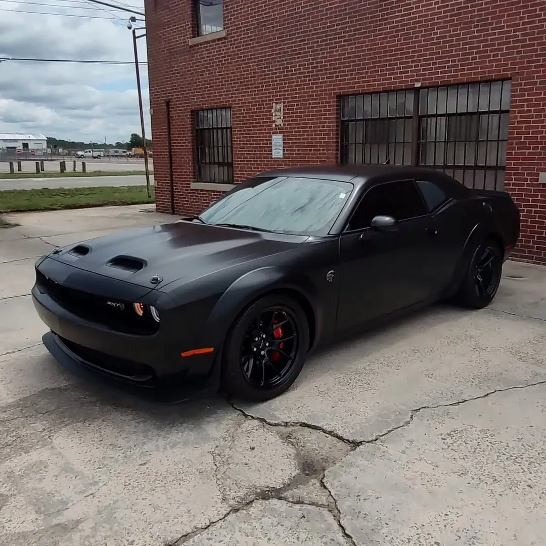 Black Dodge Challenger parked near a brick building.