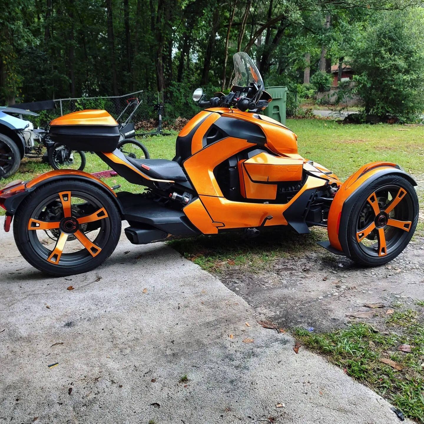 Orange and black Can-Am Ryker trike parked on a concrete surface, with a black storage box.