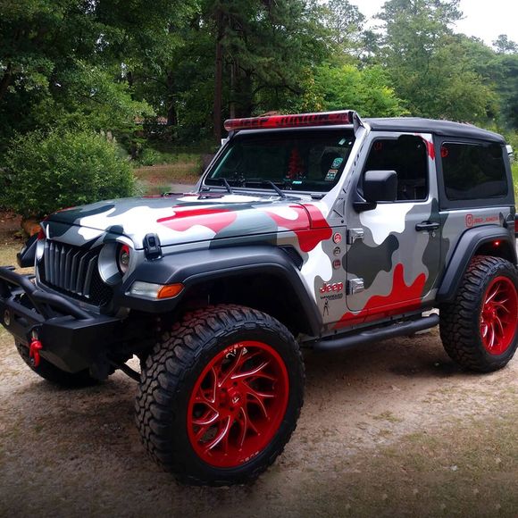 Camouflaged Jeep with red wheels, in a natural setting.