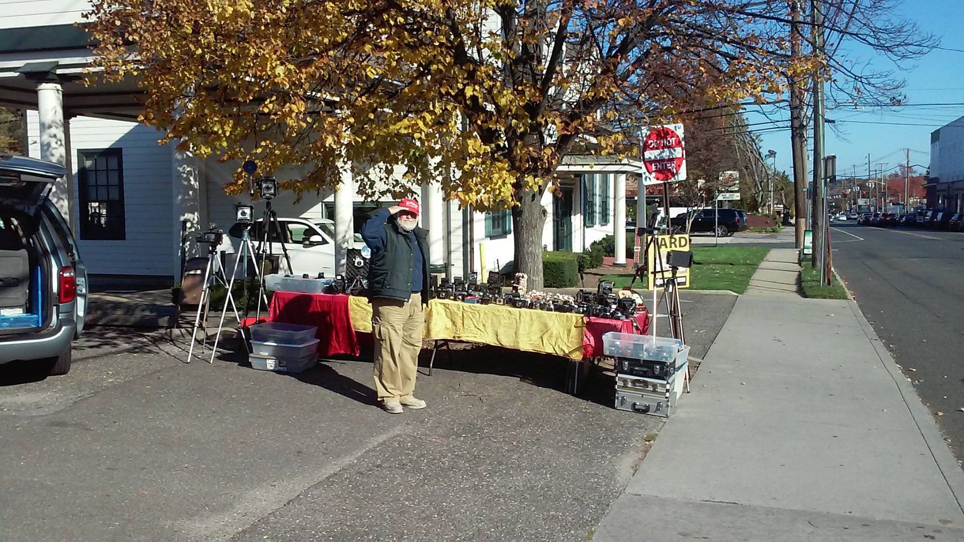 Outdoor yard sale table on a sidewalk beside a street, with autumn trees and houses in the background.