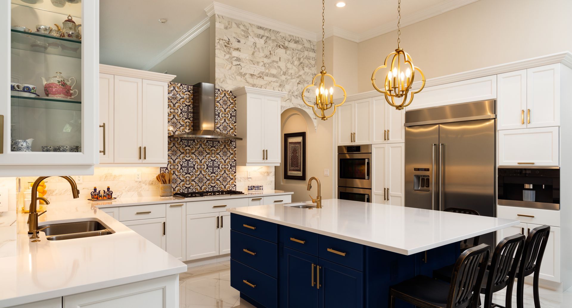 Modern kitchen with white cabinetry, a deep blue island, quartz countertops, patterned backsplash, and gold accents.