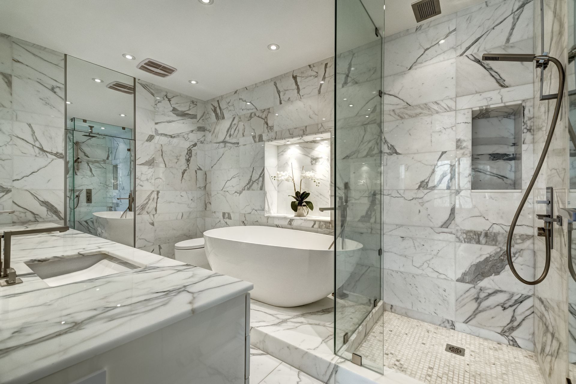 A modern luxury bathroom featuring white marble walls, a freestanding soaking tub, and a glass-enclosed walk-in shower.