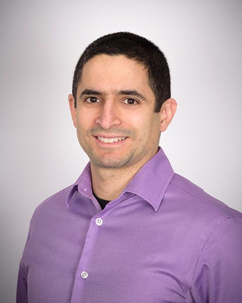Patrick Massad smiling, wearing a purple collared shirt against a white background.