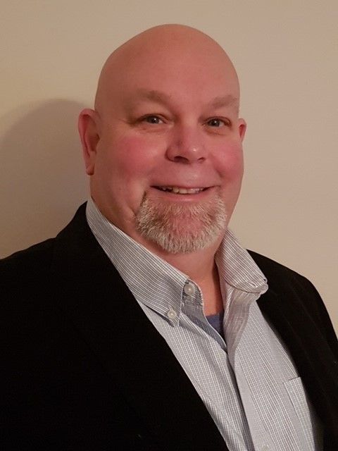 Glenn Golaz smiling in a black blazer and light blue collared shirt.