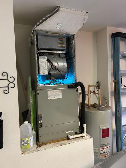 An air conditioner is sitting in a room next to a water heater.