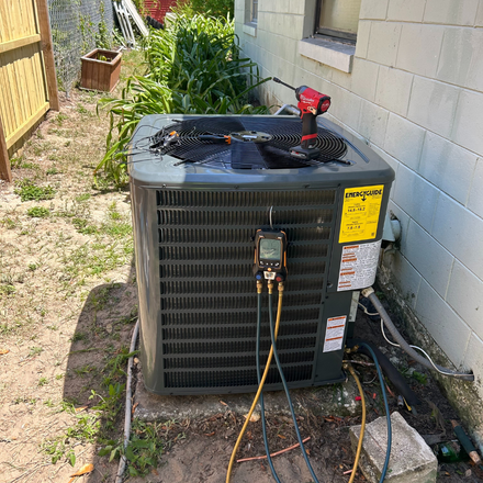 An air conditioner is sitting outside of a house with a hose attached to it.