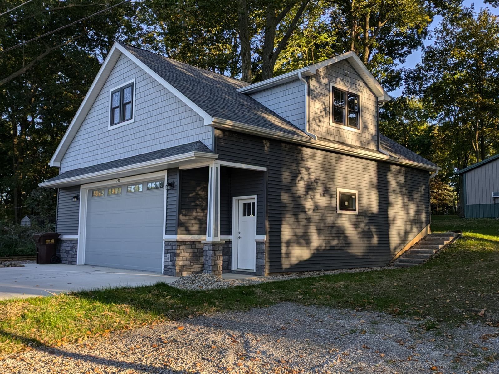Two-story garage with gray siding, gray garage door, white door, stone accents, and a grassy yard.