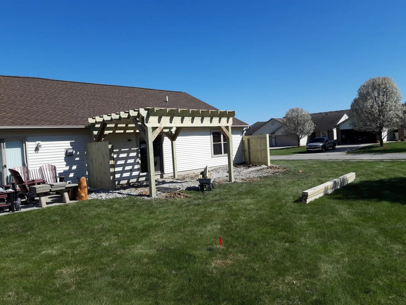 Backyard with a wooden pergola attached to a house, green grass, and a sunny blue sky.