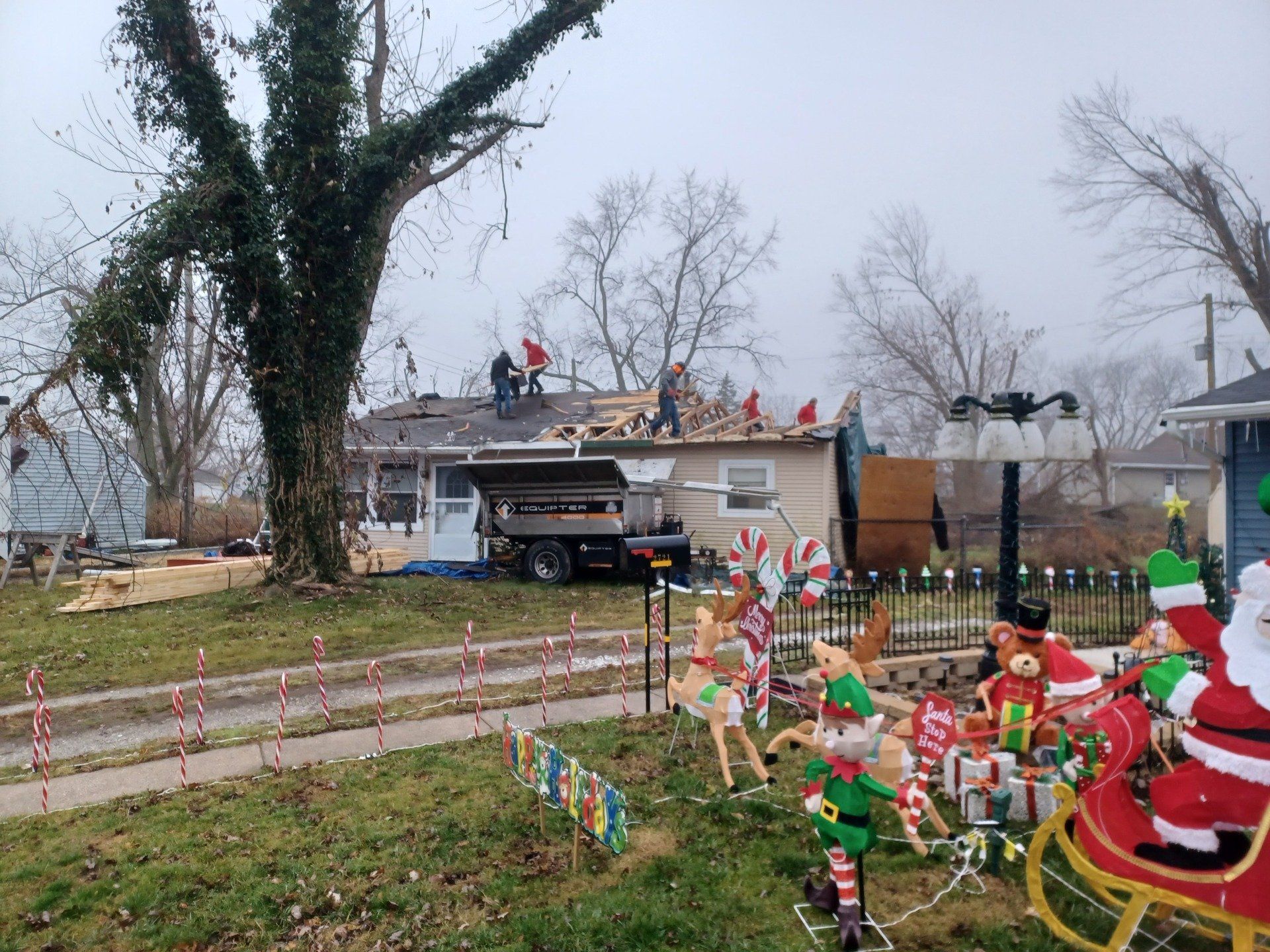 Workers replacing a roof on a house decorated with Christmas lights.
