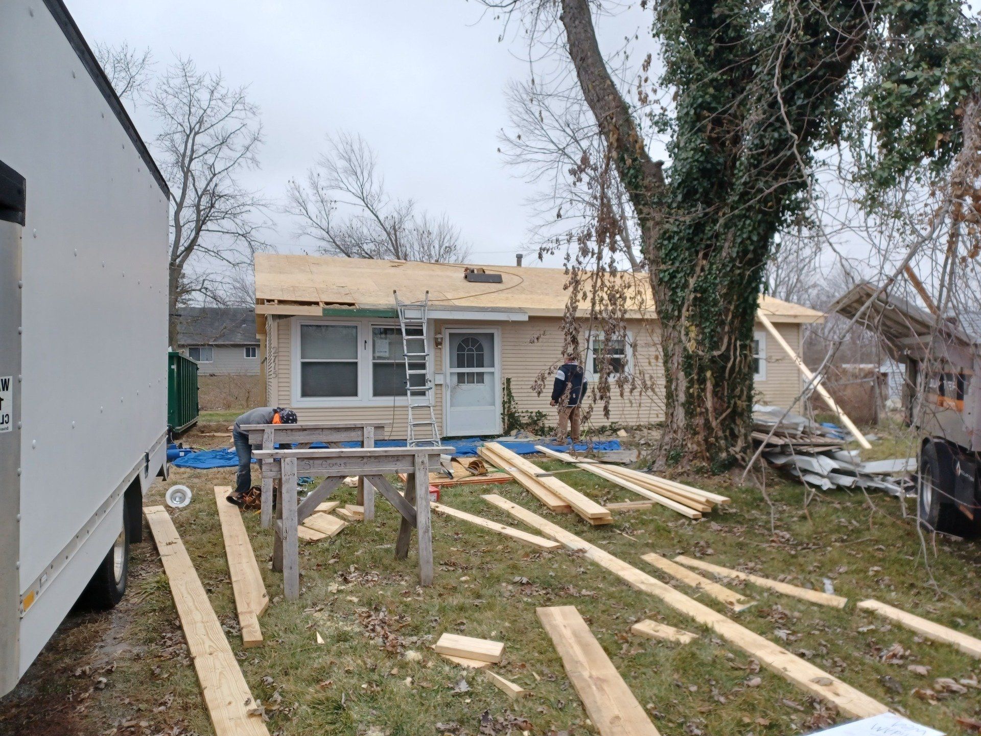 House under construction; roof work in progress; wood and tools on ground; cloudy day.