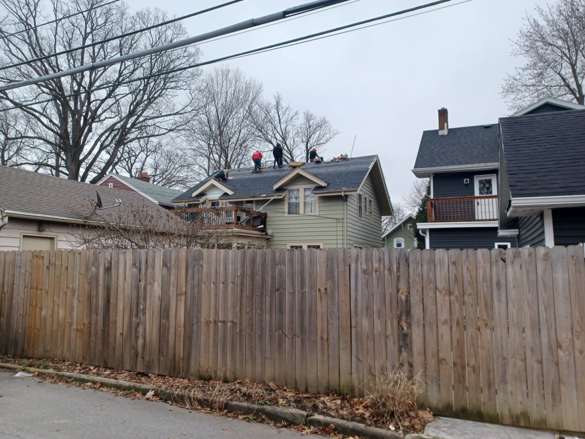 People working on a rooftop in a neighborhood, trees, wooden fences, overcast sky.