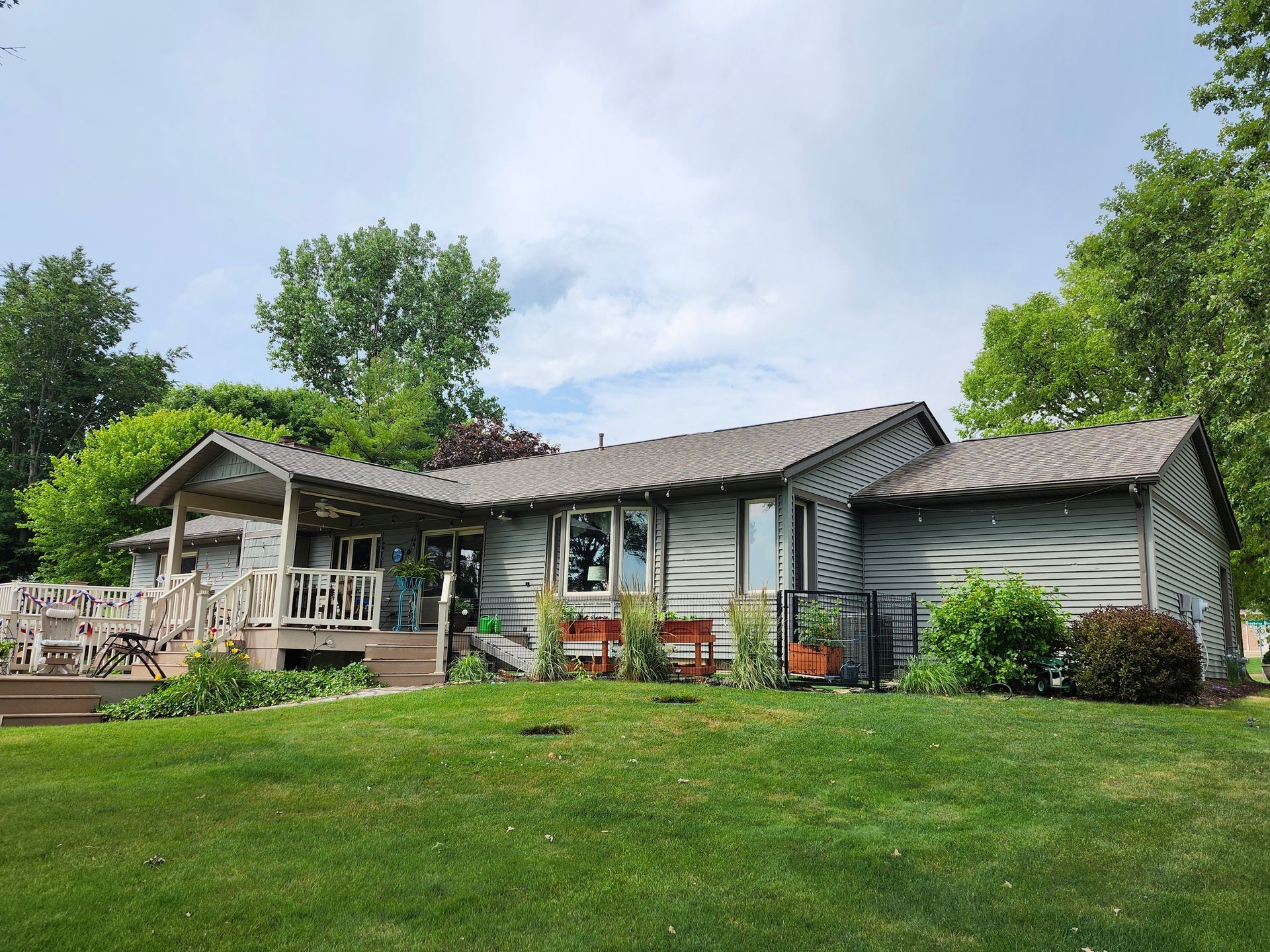 A light green house with a wooden deck and lush green lawn under a cloudy sky.