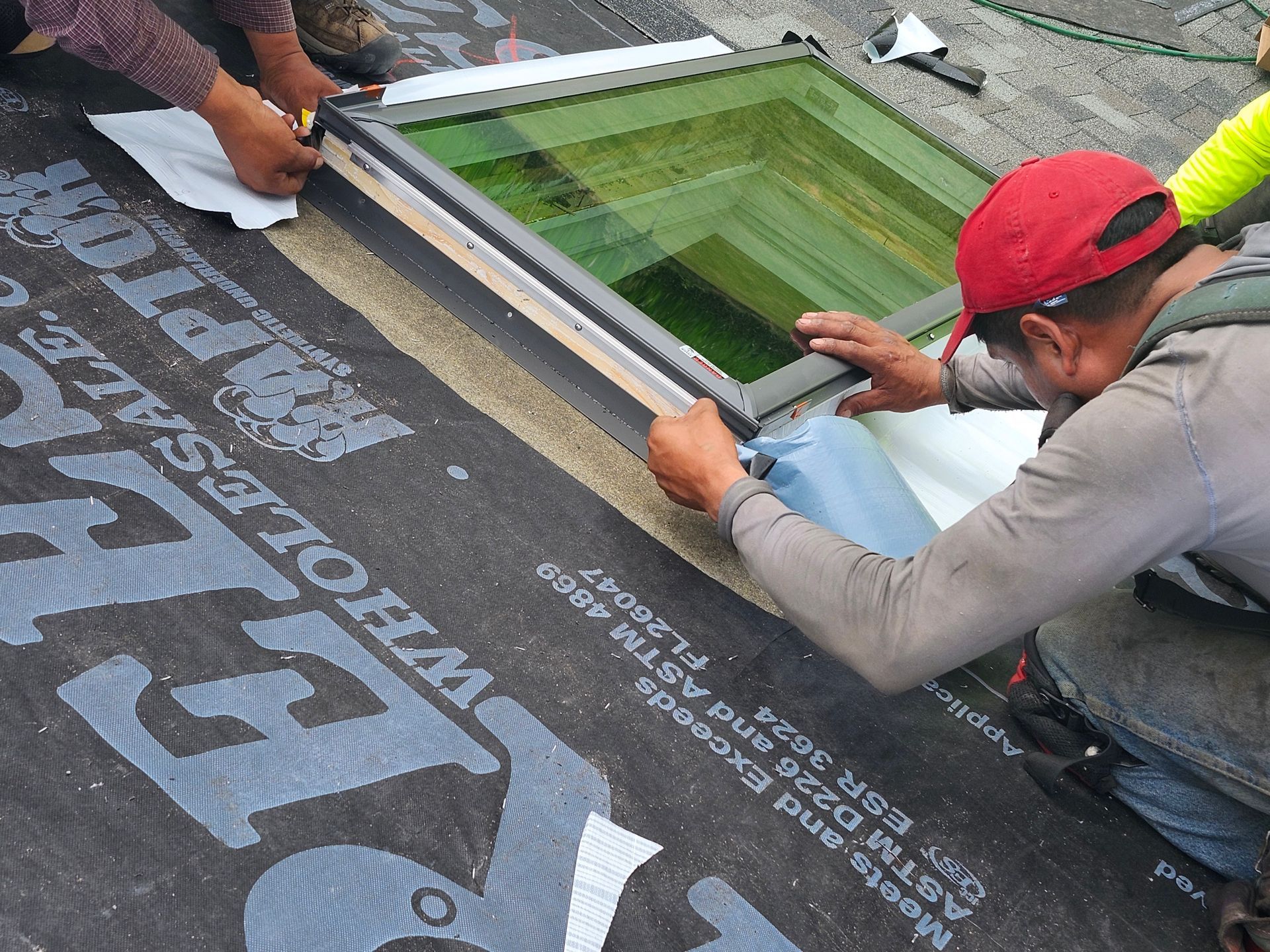 Roofers installing a skylight on a flat roof, using tools and materials.