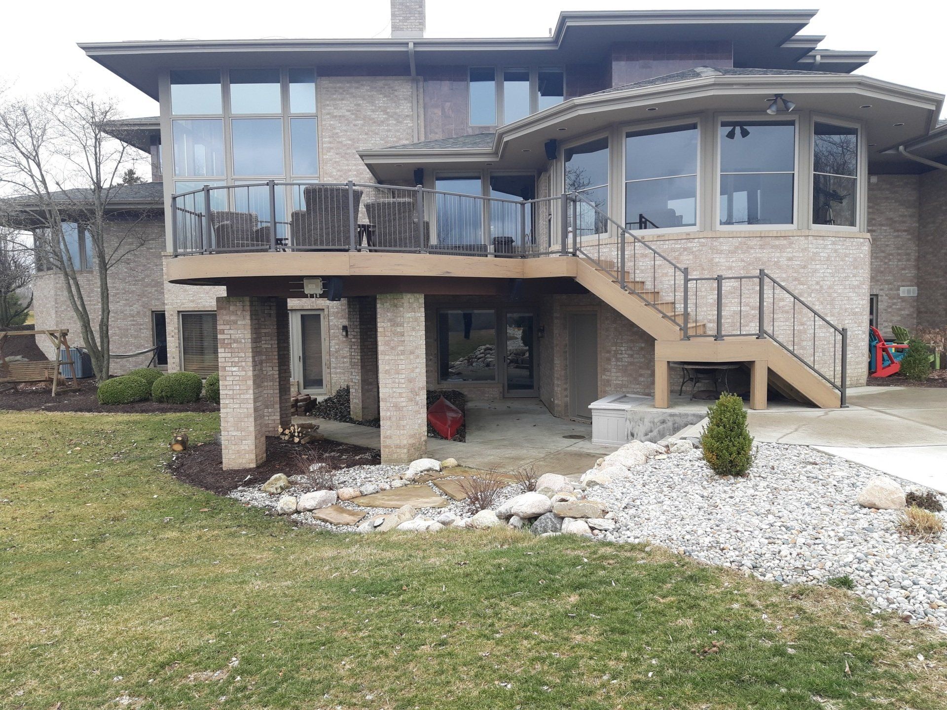 Brick house with deck and stairs, overlooking a grassy yard with a small rock garden.