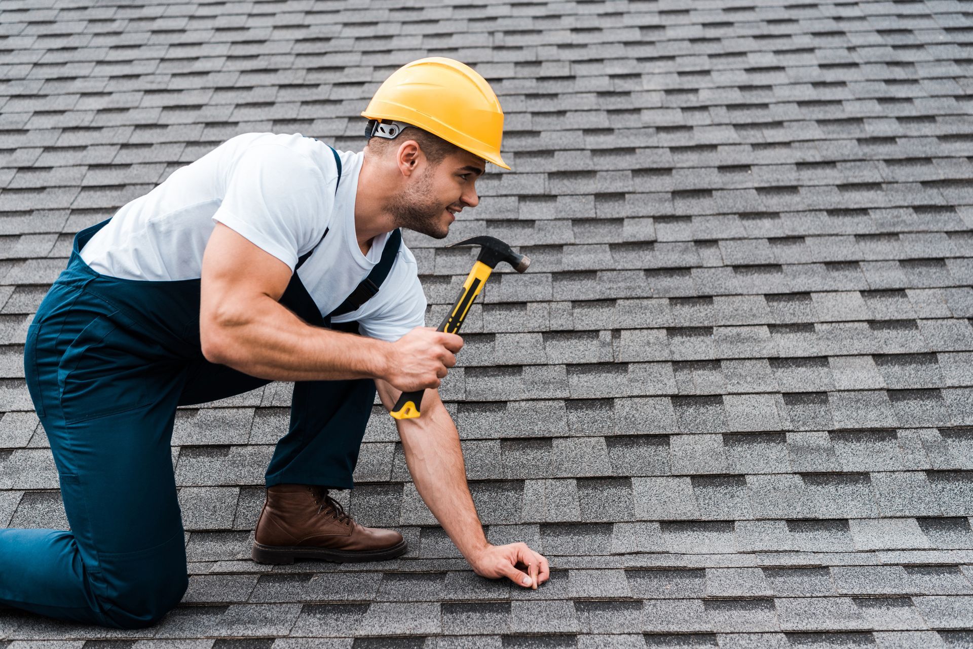 A male roof contractor hammers a roof tile with a hammer.
