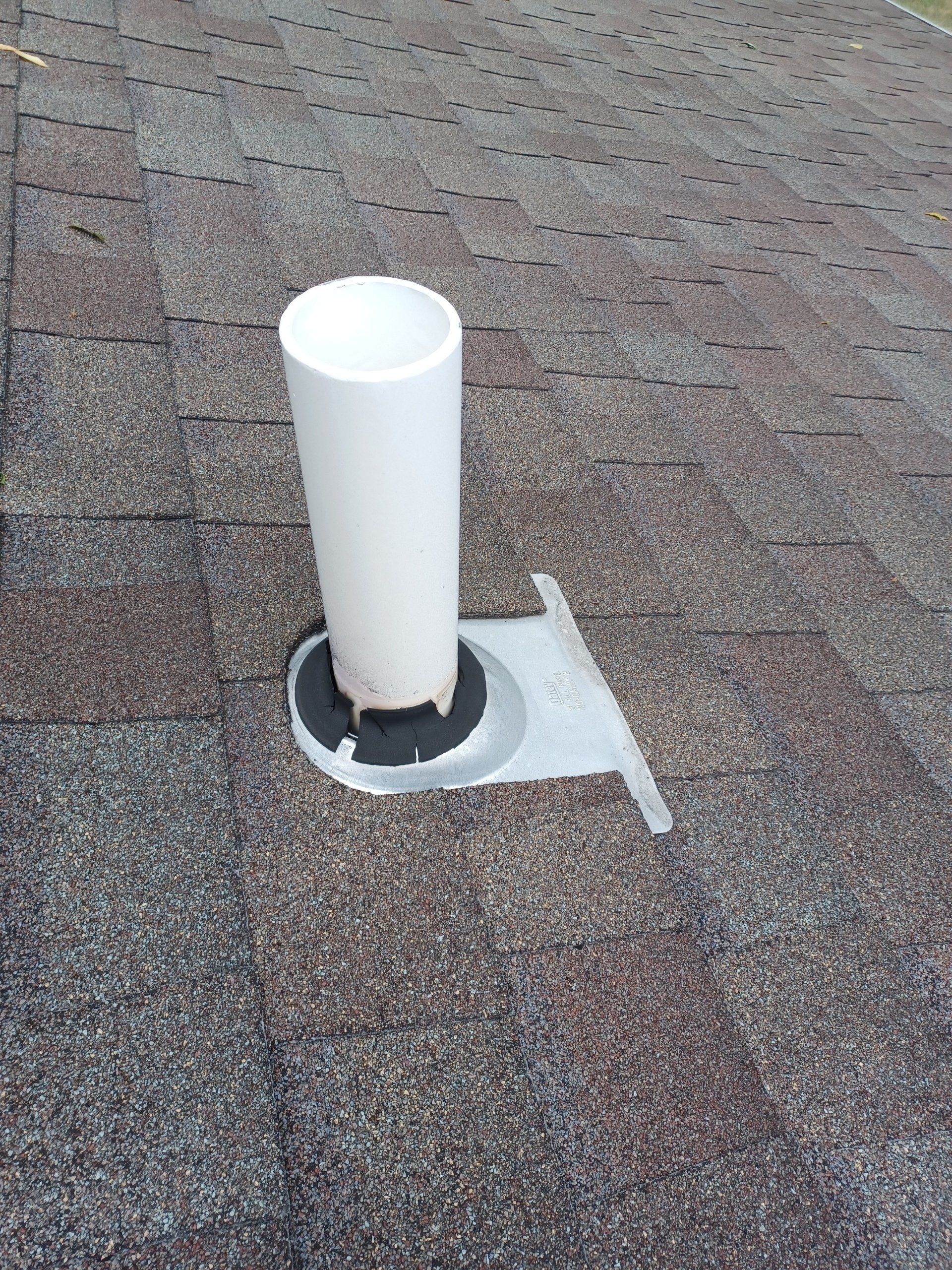 White vent pipe protruding from a roof covered in brown shingles.