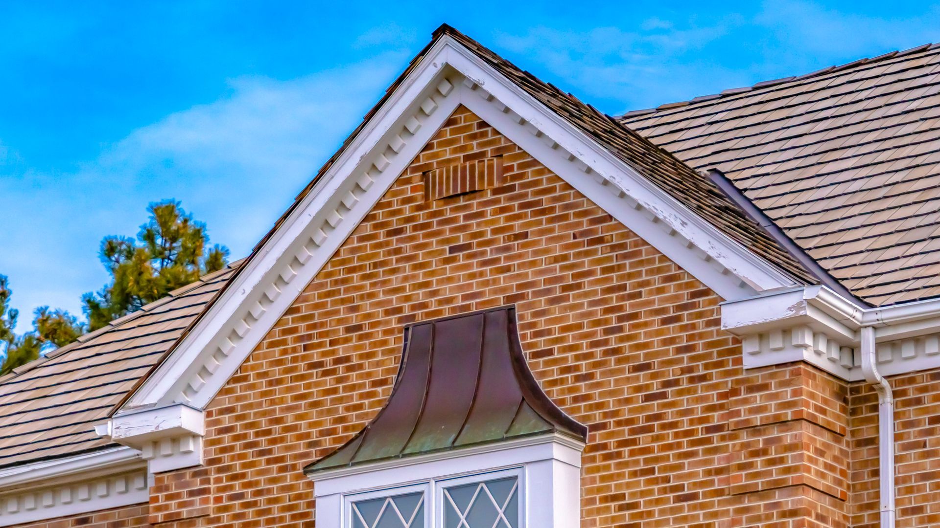 Brick house exterior with copper-toned window canopy and white trim.