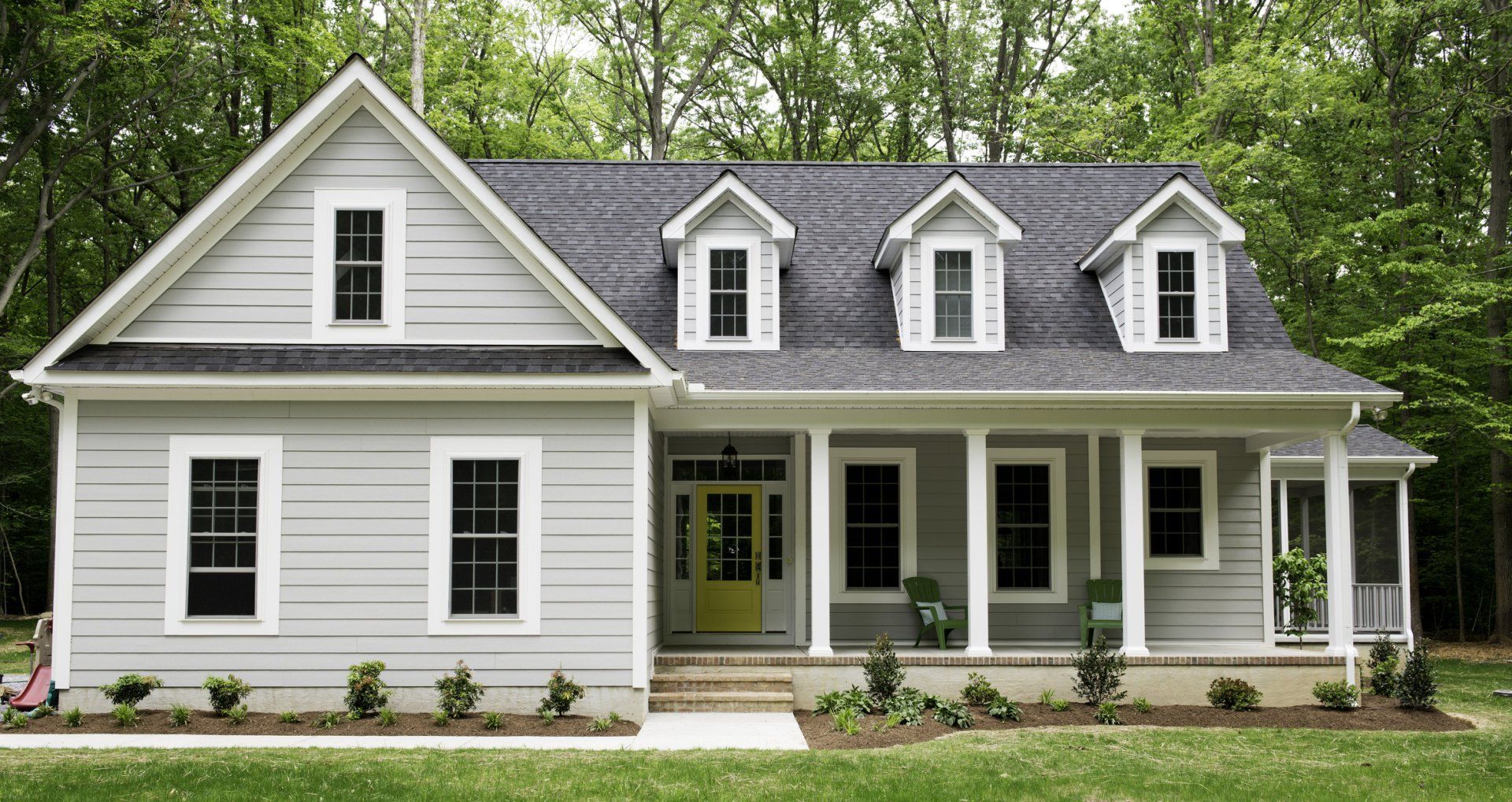 Light gray house with white trim, front porch, three dormers, and yellow front door.