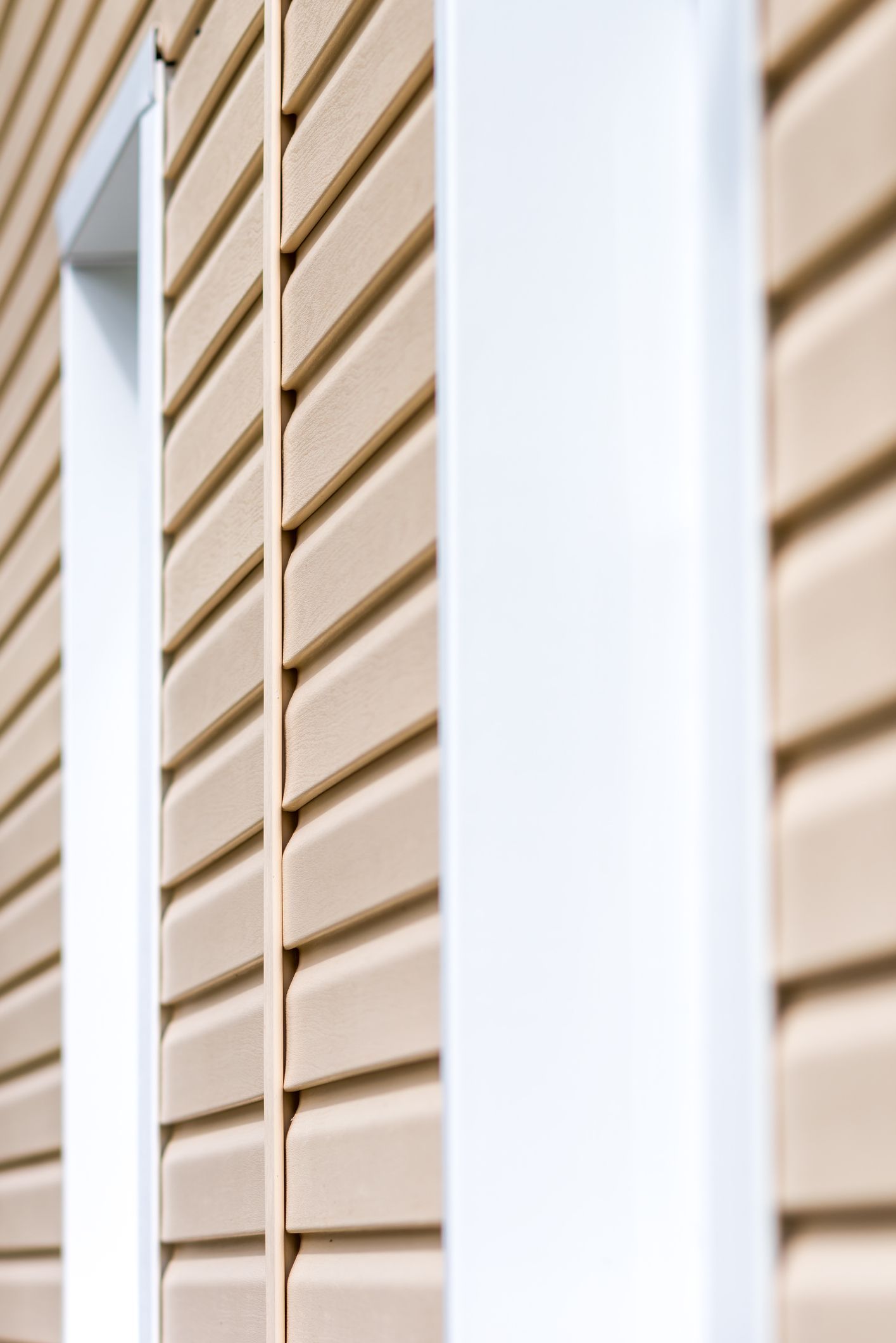 Close-up of beige vinyl siding with white fittings outside a home.