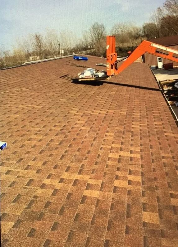 A person on a roof using a lift to install brown asphalt shingles.