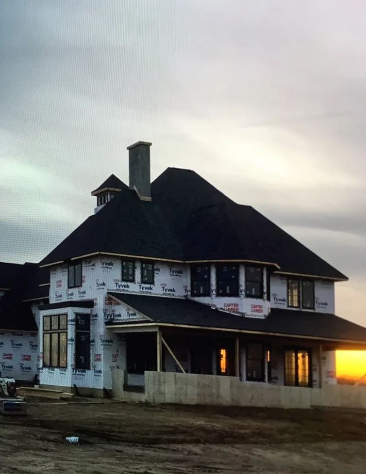House under construction, wrapped in protective paper, dark roof, cloudy sky, sunset.